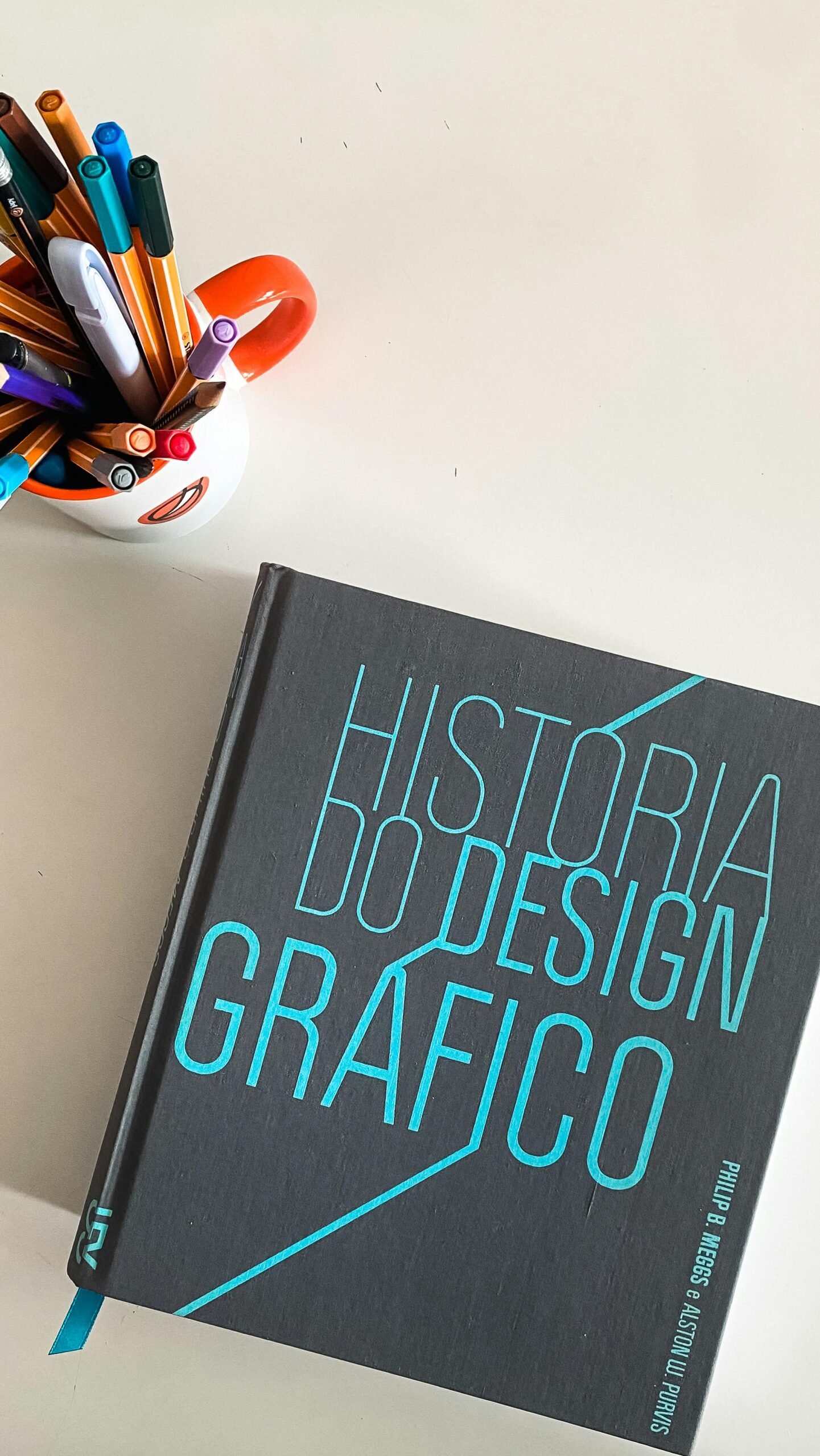 A graphic design history book and a mug of pens on a minimalist desk.